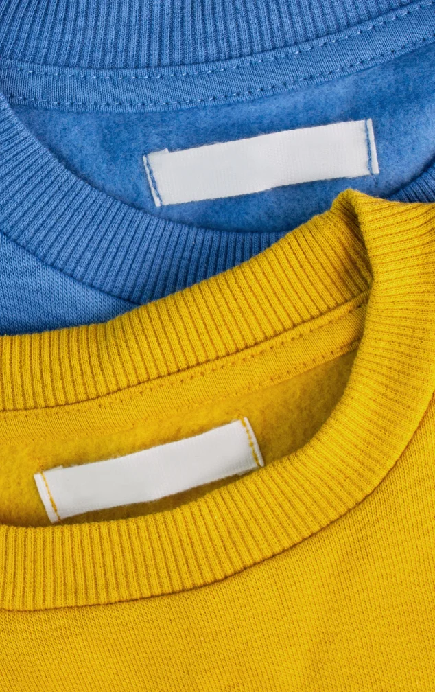 Etiquetas textiles blancas en los cuellos de sudaderas amarillas y azules, Fabricante: Etimex Digital en Mexico.